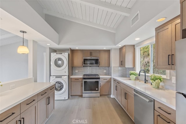 kitchen with stacked washer / dryer, appliances with stainless steel finishes, sink, hanging light fixtures, and beam ceiling