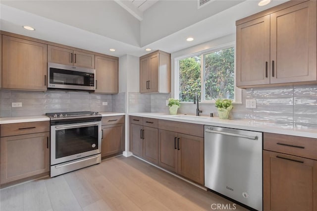 kitchen with light hardwood / wood-style flooring, appliances with stainless steel finishes, sink, tasteful backsplash, and lofted ceiling