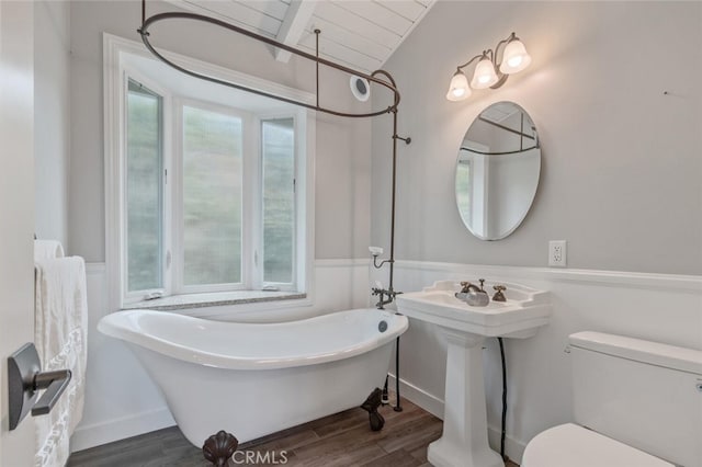 full bath with a wainscoted wall, toilet, vaulted ceiling, wood finished floors, and a soaking tub