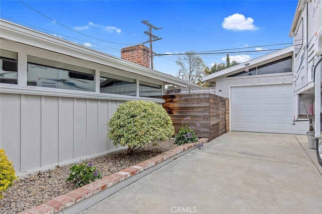 view of property exterior with a garage, board and batten siding, a chimney, and fence