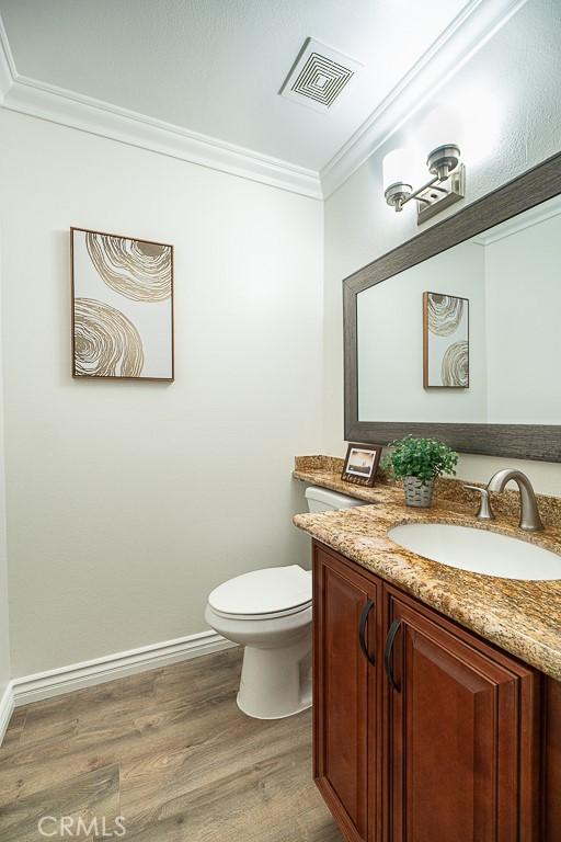 bathroom featuring toilet, ornamental molding, wood-type flooring, and vanity