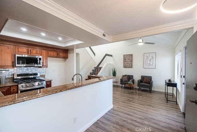 kitchen featuring ceiling fan, backsplash, dark stone countertops, crown molding, and appliances with stainless steel finishes