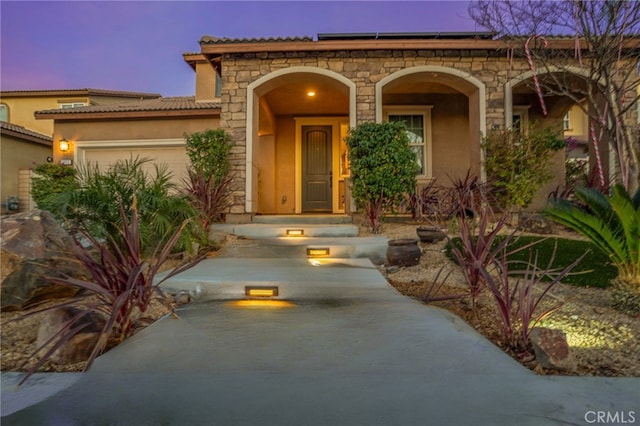 exterior entry at dusk featuring a garage and solar panels