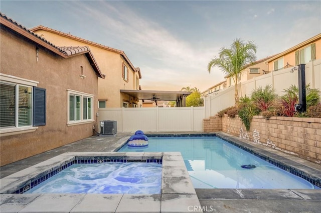 pool at dusk with cooling unit and an in ground hot tub