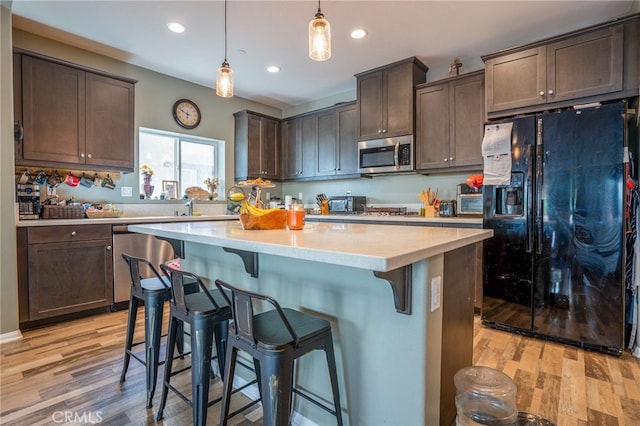 kitchen with light hardwood / wood-style floors, dark brown cabinetry, appliances with stainless steel finishes, and hanging light fixtures