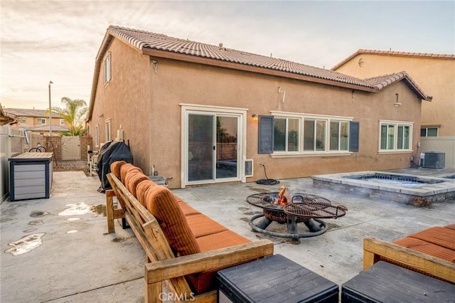 back house at dusk with an outdoor fire pit, central AC unit, a patio, and an outdoor hot tub