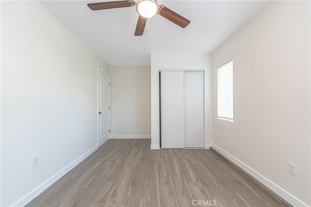 unfurnished bedroom with ceiling fan, a closet, and dark wood-type flooring