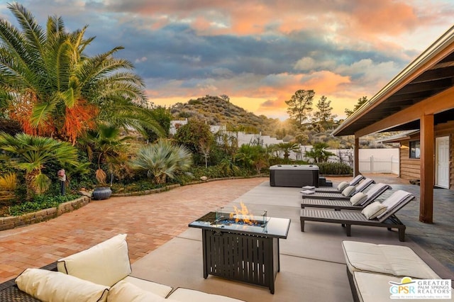 patio terrace at dusk featuring a hot tub and an outdoor living space with a fire pit