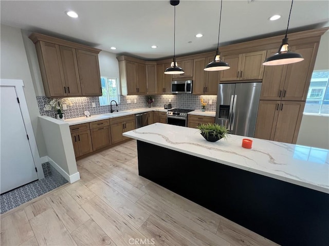 kitchen with light stone countertops, stainless steel appliances, pendant lighting, and sink