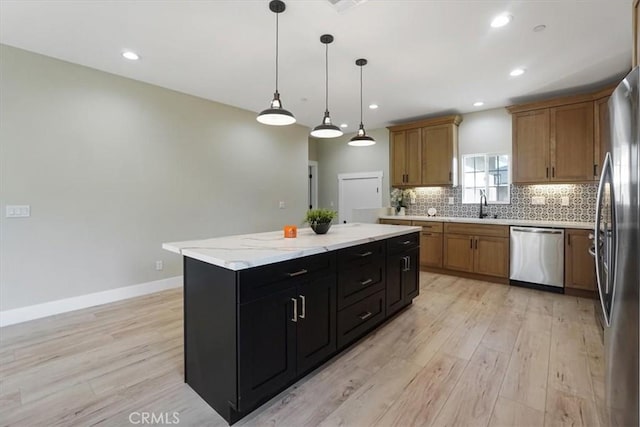 kitchen with pendant lighting, appliances with stainless steel finishes, a kitchen island, sink, and light hardwood / wood-style flooring