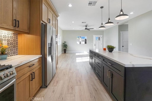 kitchen with decorative light fixtures, ceiling fan, light wood-type flooring, appliances with stainless steel finishes, and a large island