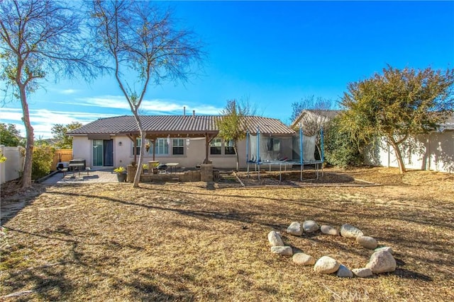 back of property featuring a trampoline, a patio area, stucco siding, and a fenced backyard