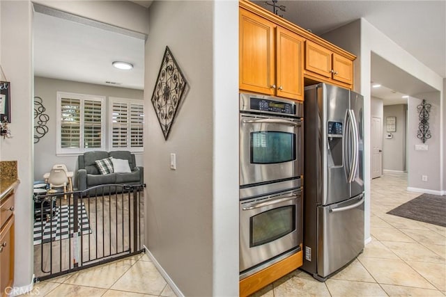 kitchen featuring stainless steel appliances, light tile patterned floors, baseboards, and brown cabinets