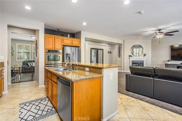 kitchen featuring an island with sink, appliances with stainless steel finishes, light tile patterned flooring, a sink, and open floor plan