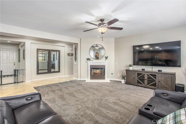 carpeted living area featuring a glass covered fireplace, tile patterned floors, baseboards, and a ceiling fan
