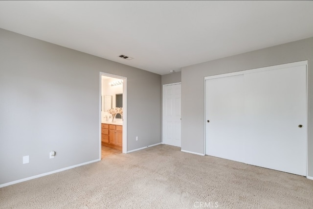 unfurnished bedroom featuring light colored carpet, ensuite bath, and a closet