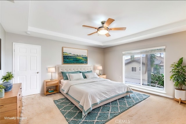 carpeted bedroom with ceiling fan and a tray ceiling