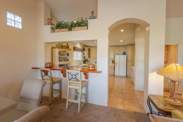 kitchen featuring a kitchen breakfast bar, light tile patterned flooring, white refrigerator with ice dispenser, and a high ceiling