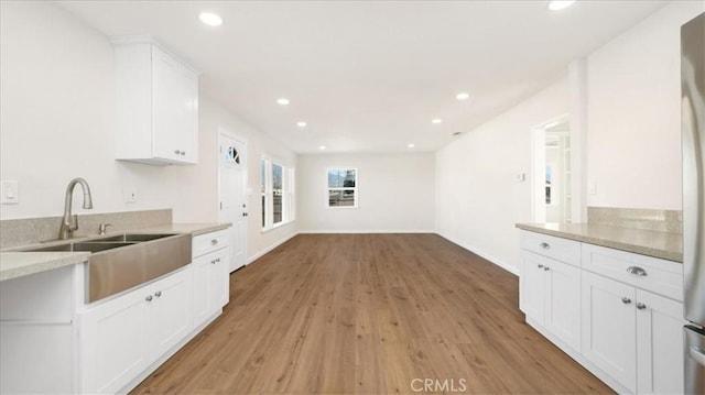 kitchen with light hardwood / wood-style floors, white cabinets, light stone counters, and sink