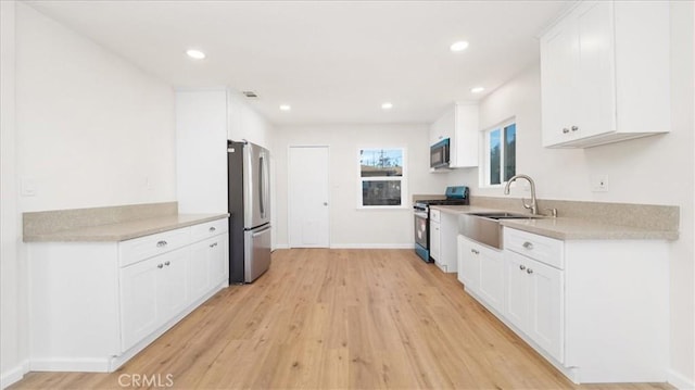 kitchen with light wood-type flooring, stainless steel appliances, white cabinets, and sink