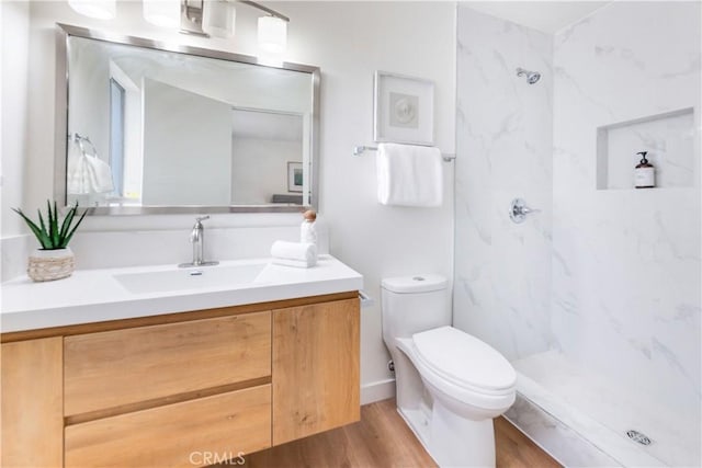 bathroom featuring vanity, tiled shower, hardwood / wood-style floors, and toilet