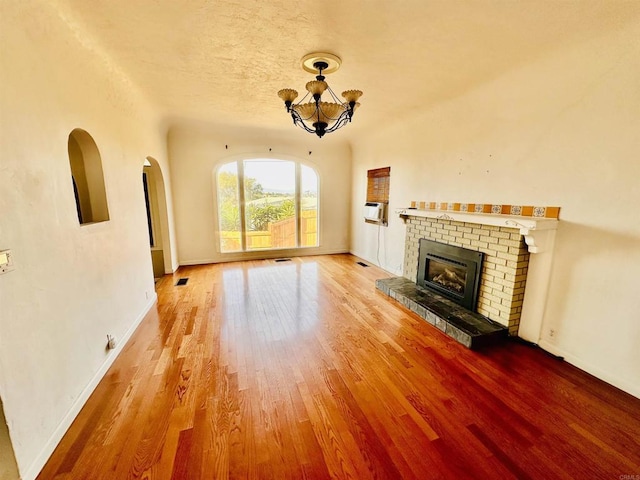 unfurnished living room with a brick fireplace, hardwood / wood-style flooring, and a notable chandelier