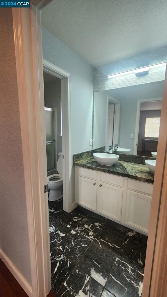 bathroom with an enclosed shower, vanity, toilet, and a textured ceiling