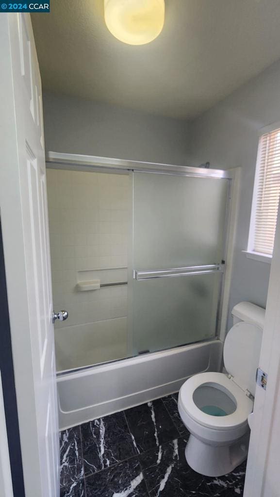 bathroom featuring combined bath / shower with glass door and toilet