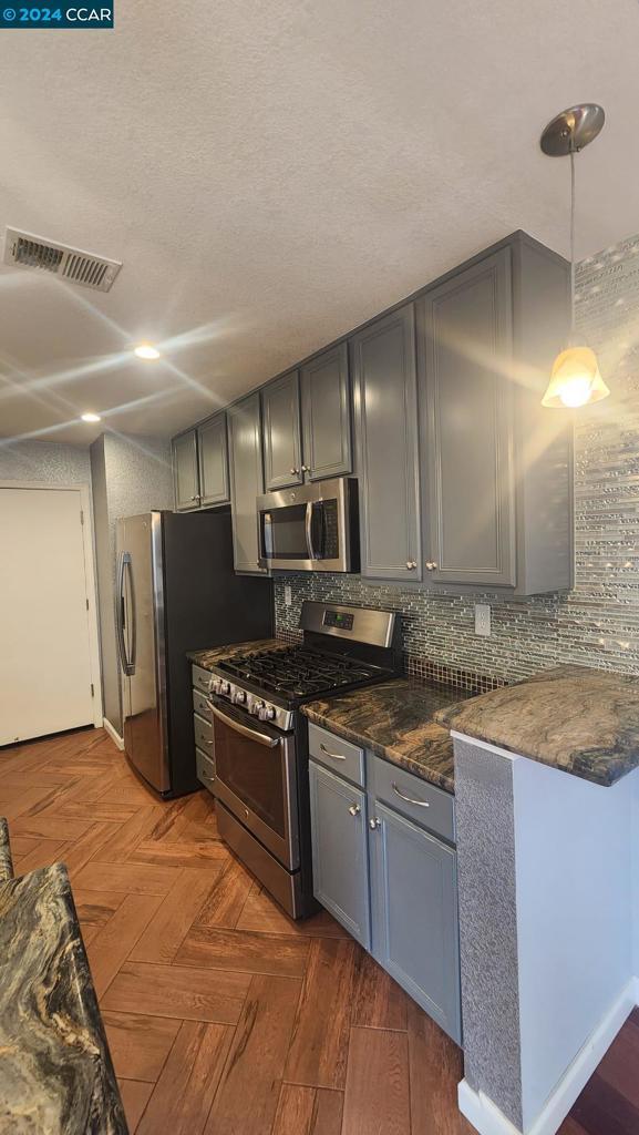 kitchen featuring dark stone countertops, pendant lighting, dark parquet floors, gray cabinetry, and stainless steel appliances