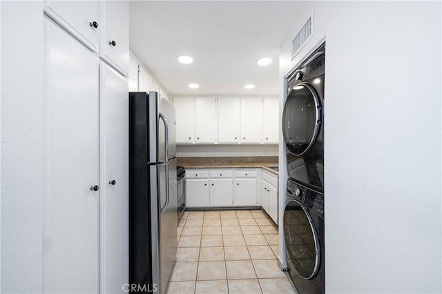 kitchen featuring stacked washing maching and dryer, appliances with stainless steel finishes, light tile patterned flooring, and white cabinetry