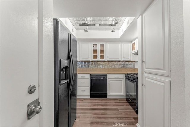 kitchen with white cabinets, black appliances, wood-type flooring, tasteful backsplash, and rail lighting