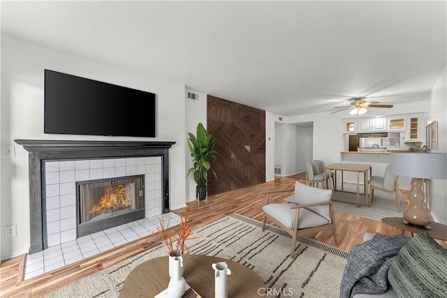 living room featuring a tile fireplace, ceiling fan, and light hardwood / wood-style floors