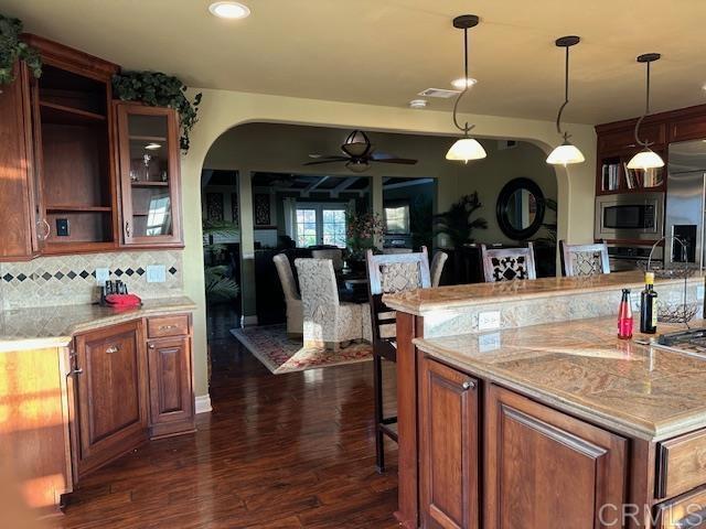 kitchen with appliances with stainless steel finishes, a center island, dark wood-type flooring, tasteful backsplash, and ceiling fan