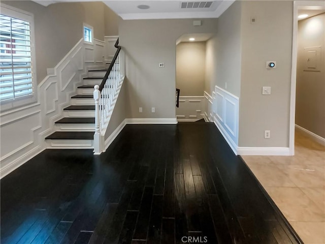 interior space featuring wood finished floors, baseboards, arched walkways, ornamental molding, and a decorative wall