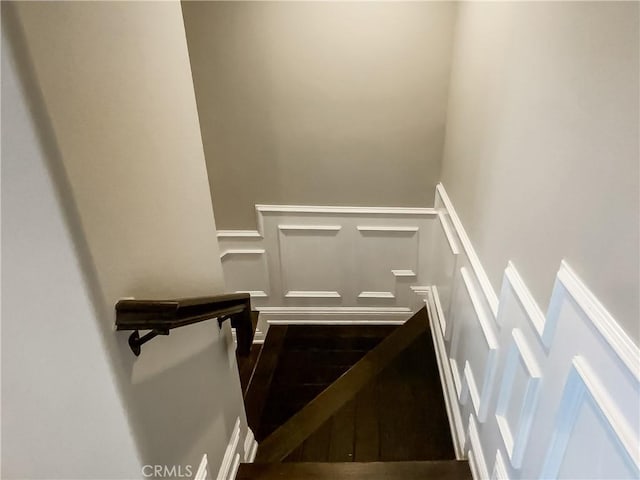 stairway with a decorative wall, wood finished floors, and wainscoting