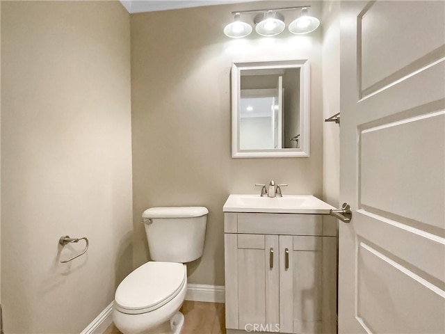 half bathroom with vanity, toilet, and baseboards