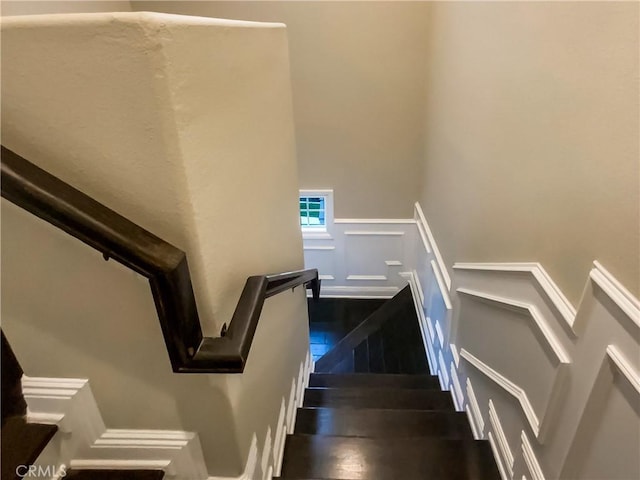 stairs featuring a wainscoted wall, wood finished floors, and a decorative wall