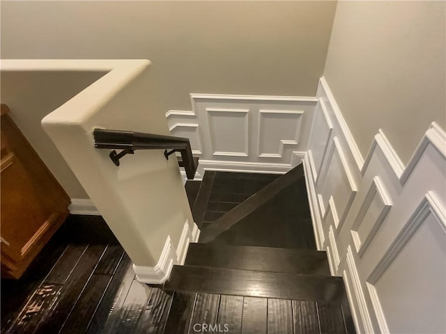 stairs featuring hardwood / wood-style floors, a decorative wall, and wainscoting