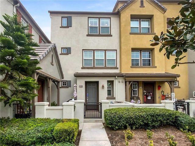 townhome / multi-family property featuring a fenced front yard, stucco siding, and a gate