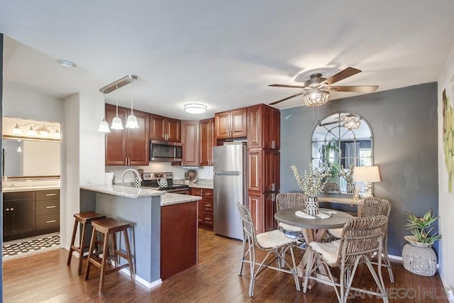 kitchen with kitchen peninsula, stainless steel appliances, dark hardwood / wood-style floors, hanging light fixtures, and light stone counters