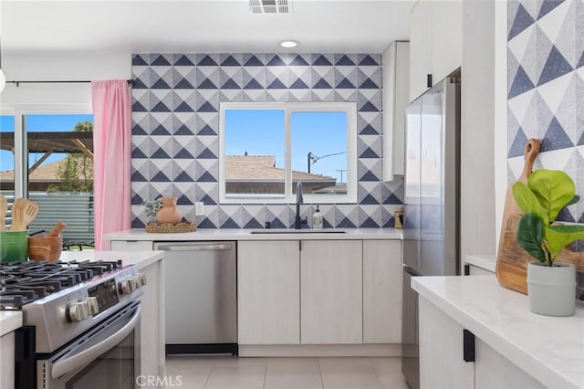 kitchen with a wealth of natural light, sink, light stone counters, and stainless steel appliances