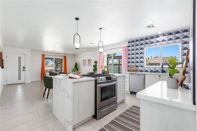 kitchen featuring decorative light fixtures, a center island, a wealth of natural light, white cabinetry, and appliances with stainless steel finishes