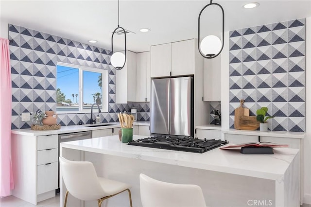 kitchen with white cabinetry, appliances with stainless steel finishes, pendant lighting, light stone counters, and sink