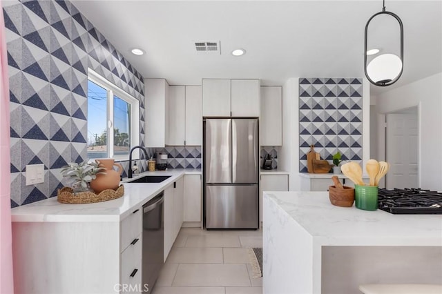 kitchen featuring sink, light tile patterned floors, hanging light fixtures, appliances with stainless steel finishes, and white cabinets