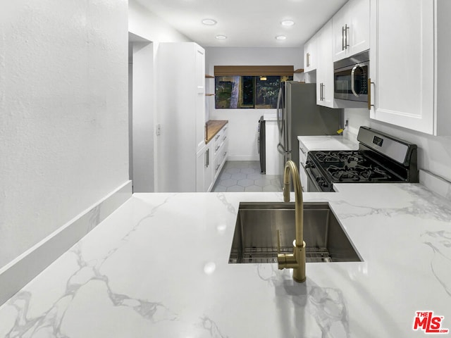 kitchen with light stone countertops, sink, stainless steel appliances, and white cabinetry