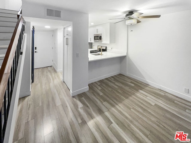 kitchen with kitchen peninsula, ceiling fan, white cabinets, range, and light hardwood / wood-style flooring