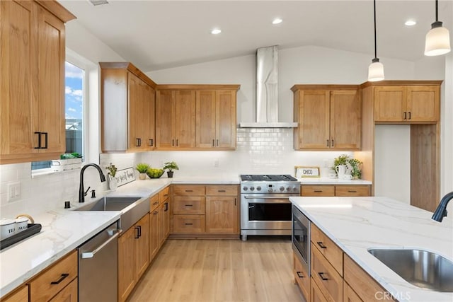 kitchen with vaulted ceiling, appliances with stainless steel finishes, sink, and wall chimney exhaust hood