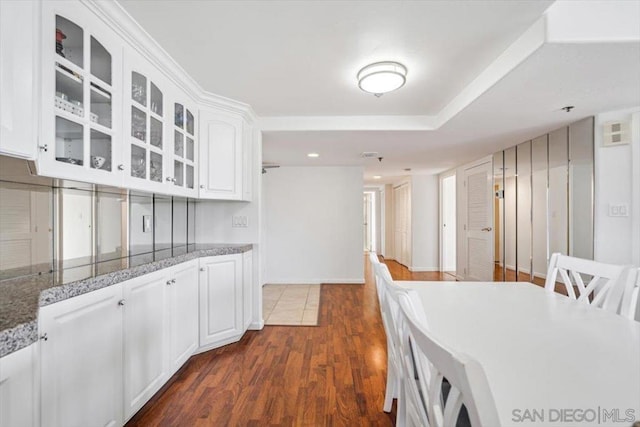 kitchen featuring dark wood-type flooring, dark stone countertops, and white cabinets