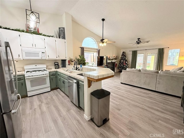 kitchen with appliances with stainless steel finishes, vaulted ceiling, sink, white cabinetry, and tile counters