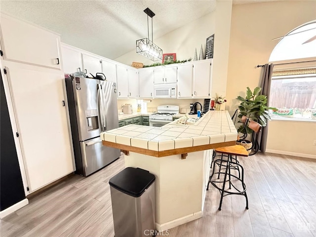 kitchen featuring a kitchen breakfast bar, white appliances, pendant lighting, tile countertops, and white cabinetry